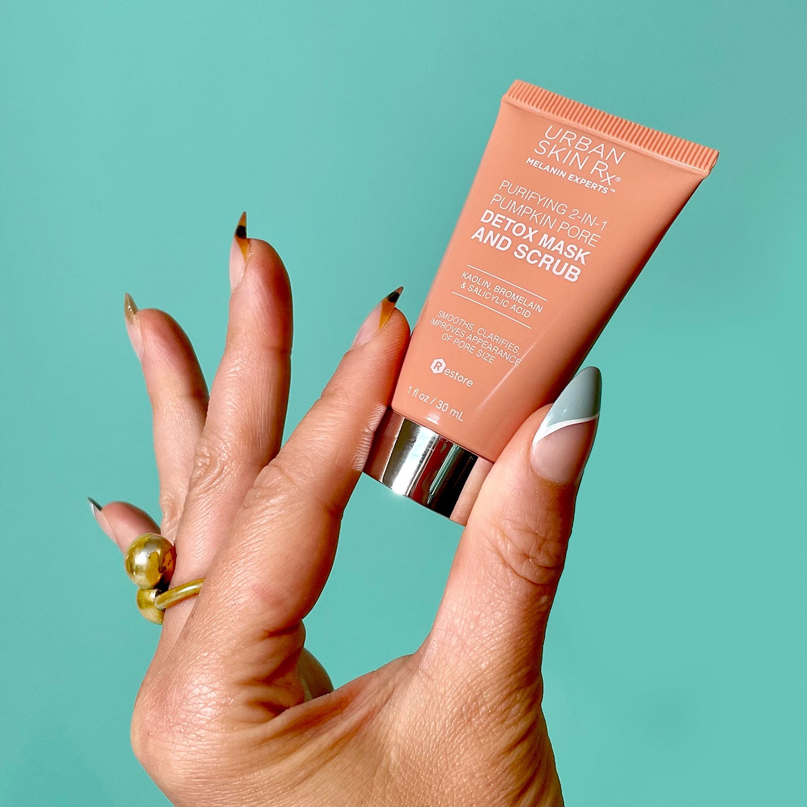 Hand holding a tube of Urban Skin Rx travel size Purifying 2-in-1 Pumpkin Mask and Scrub.