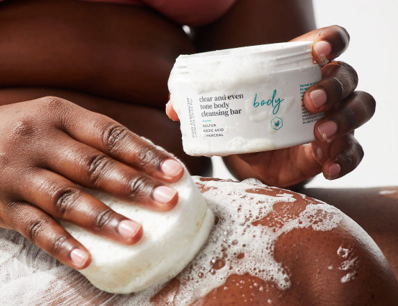 Woman holding jar of Urban Skin RX clear and even tone body cleansing bar and applying on skin