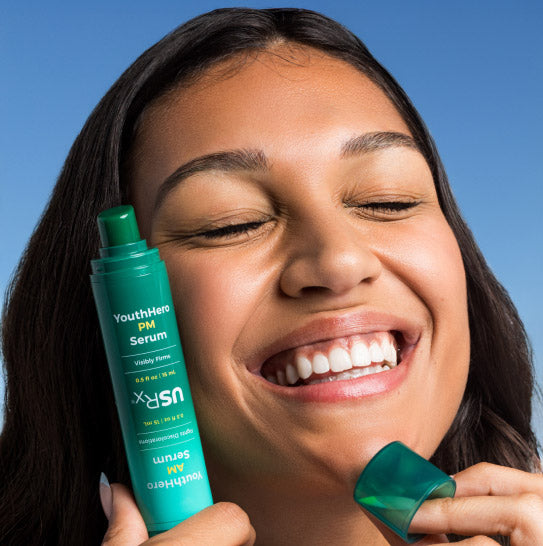 Woman holding a bottle of YouthHero PM Serum against a blue background