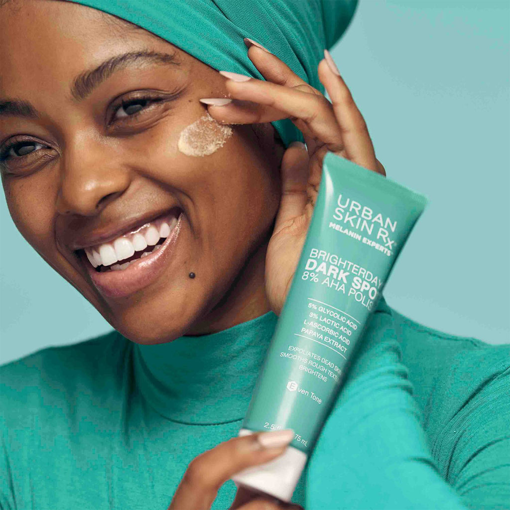 Diverse model of deep complexion holding the BrighterDays™ Dark Spot 8% AHA polish near her face while smiling
