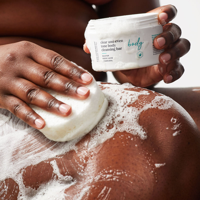Woman lathering suds from jar of USRX Clear and Even Tone Body Cleansing Bar