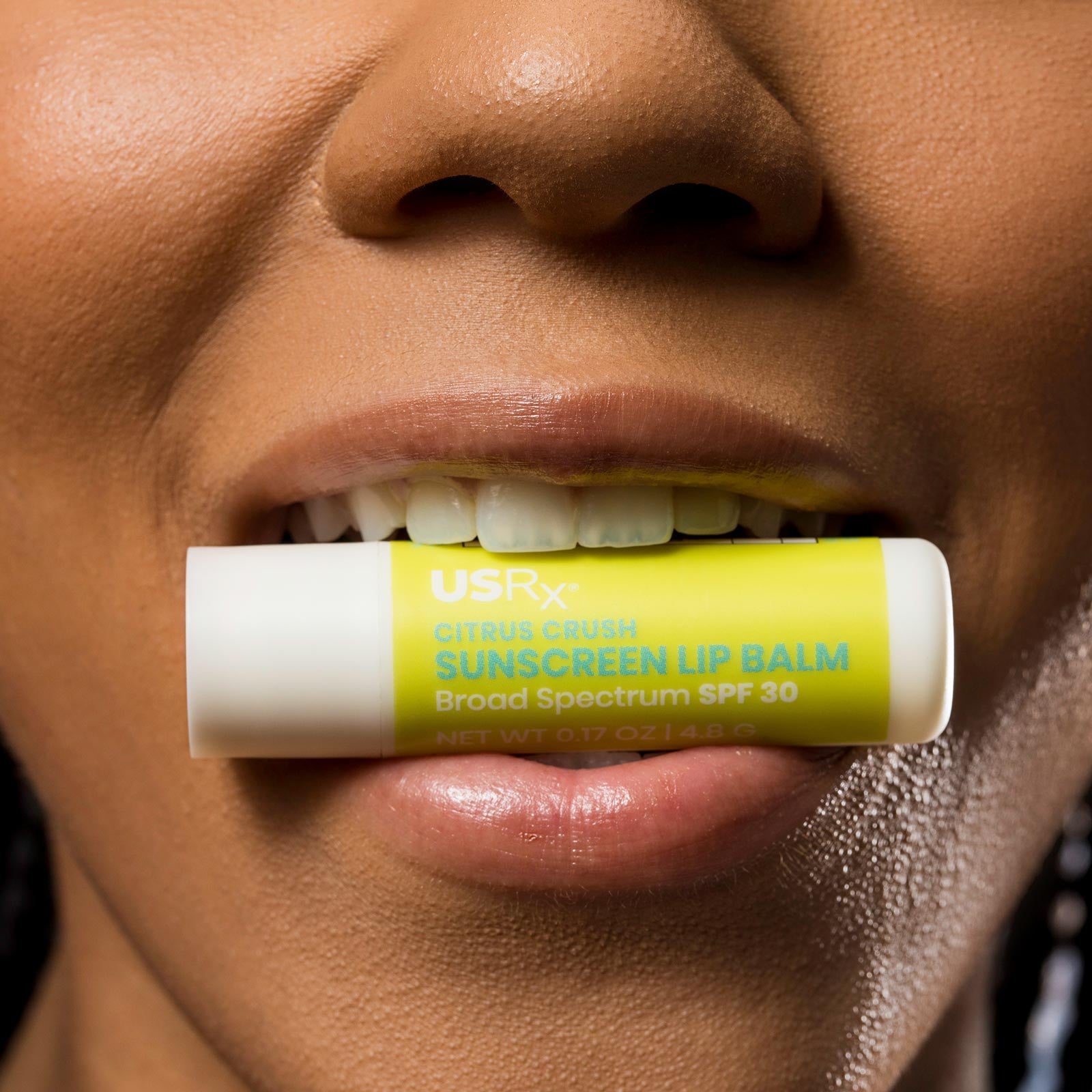 Woman holding stick of Urban Skin RX Sunscreen Lip Balm between her teeth