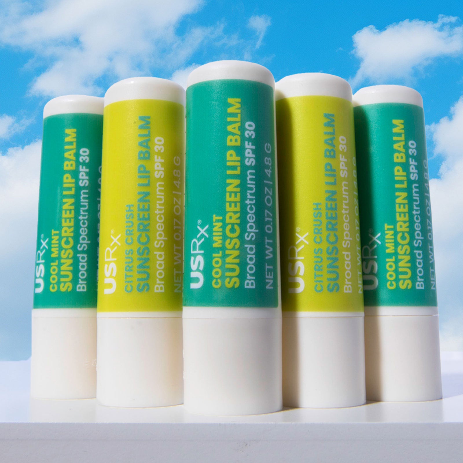 5 sticks of USRX Sunscreen Lip Balm SPF 30 set against a light blue sky background