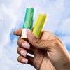 Woman holding tubes of USRx Sunscreen Lip Balm on a light blue background