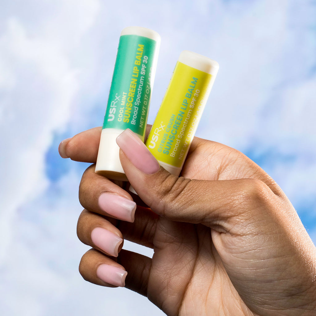 Woman holding tubes of USRx Sunscreen Lip Balm on a light blue background