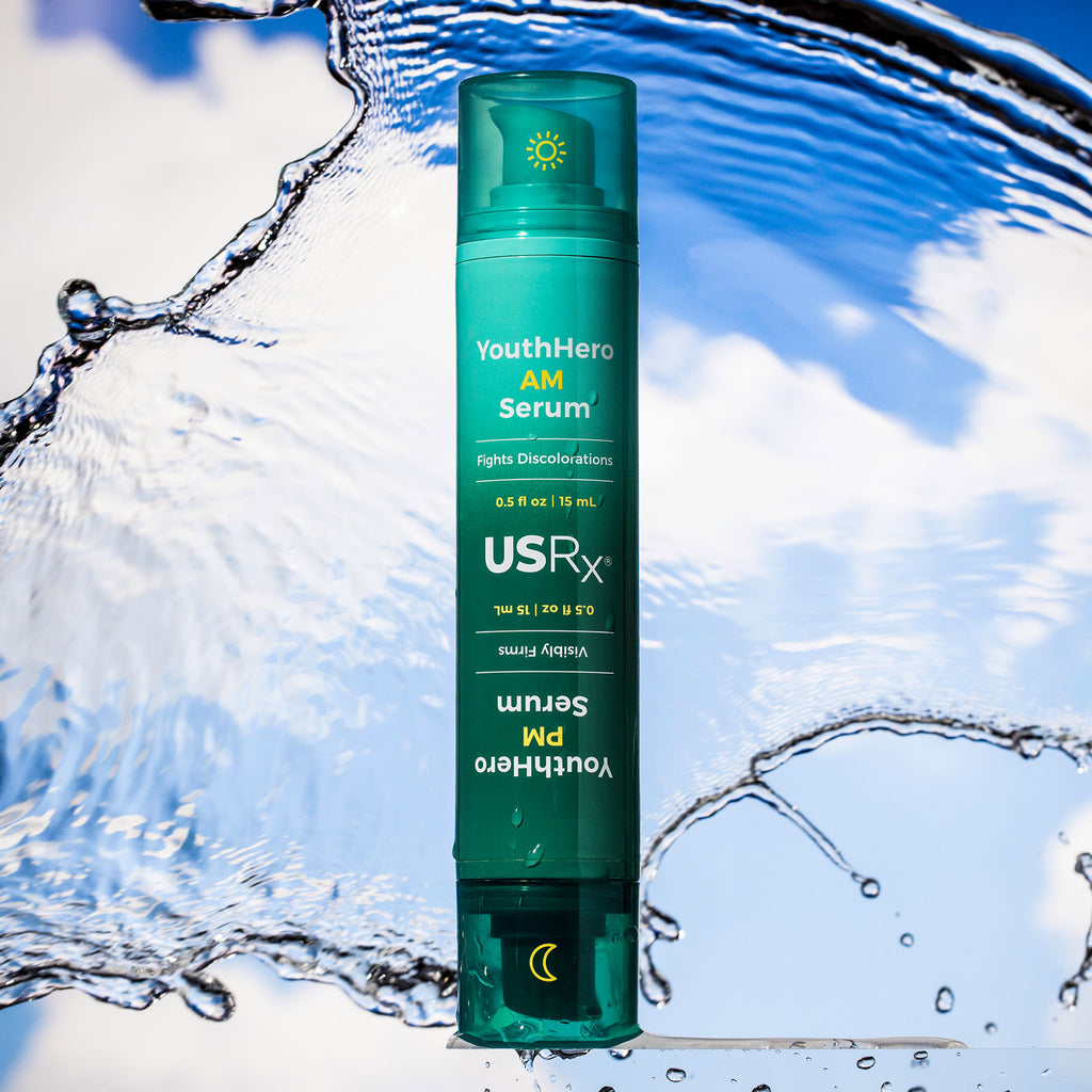 Bottle of USRx YouthHero AM/PM Serum on a blue background with a clear layer of water behind product