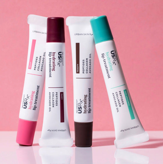 Multiple tubes of USRx Hydrating Lip Treatment in various tinted shades on a pink background