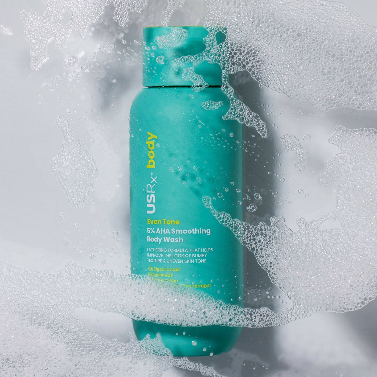 Bottle of USRx Even Tone 5% AHA Smoothing Body Wash surrounded by suds