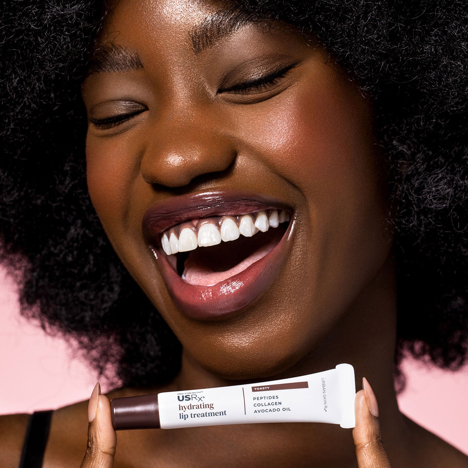 Smiling woman holding a tube of USRx Tinted Hydrating Lip Treatment in Toasty