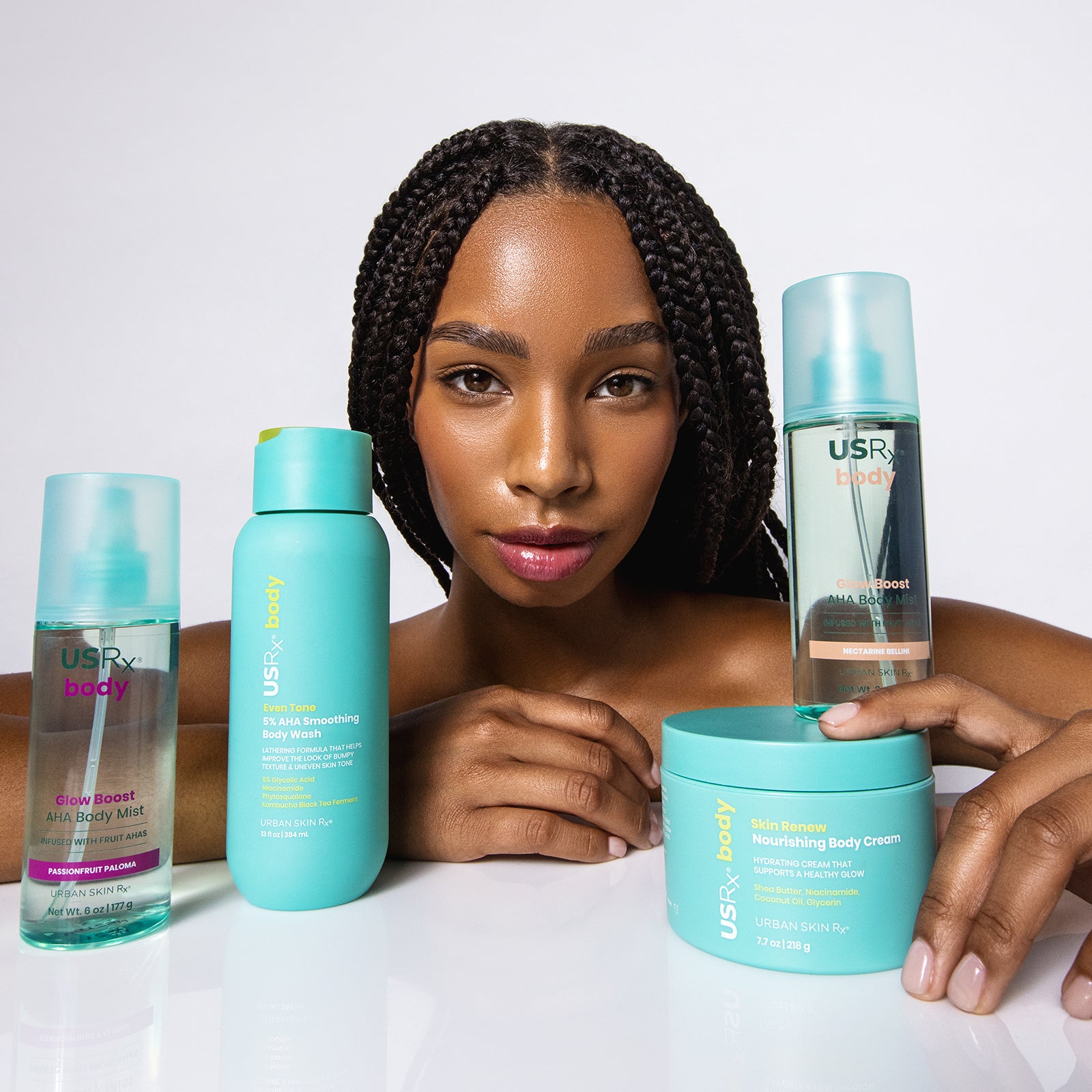 Woman beside USRx Body Hydration Bundle including Nourishing Body Cream, Glow Boost AHA Body Mist and Smoothing Body Wash
