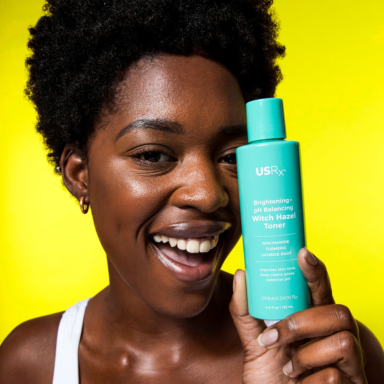 Woman holding a bottle of USRx Witch hazel toner on a yellow background