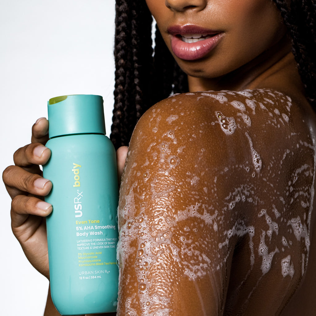Woman holding a bottle of USRx Smoothing Body Wash with suds on her upper arm