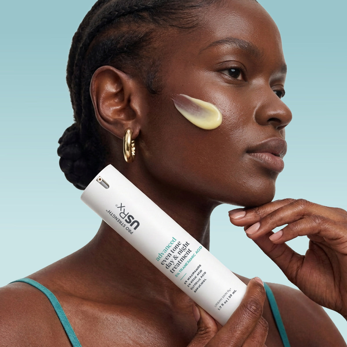 Woman holding a bottle of USRx Advanced Even Tone Day & Night Treatment near her face with a swatch of product on her cheek