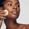African American model rubbing her face with Clear & EvenTone Clarifying Glycolic Pads which exfoliate dead skin cells